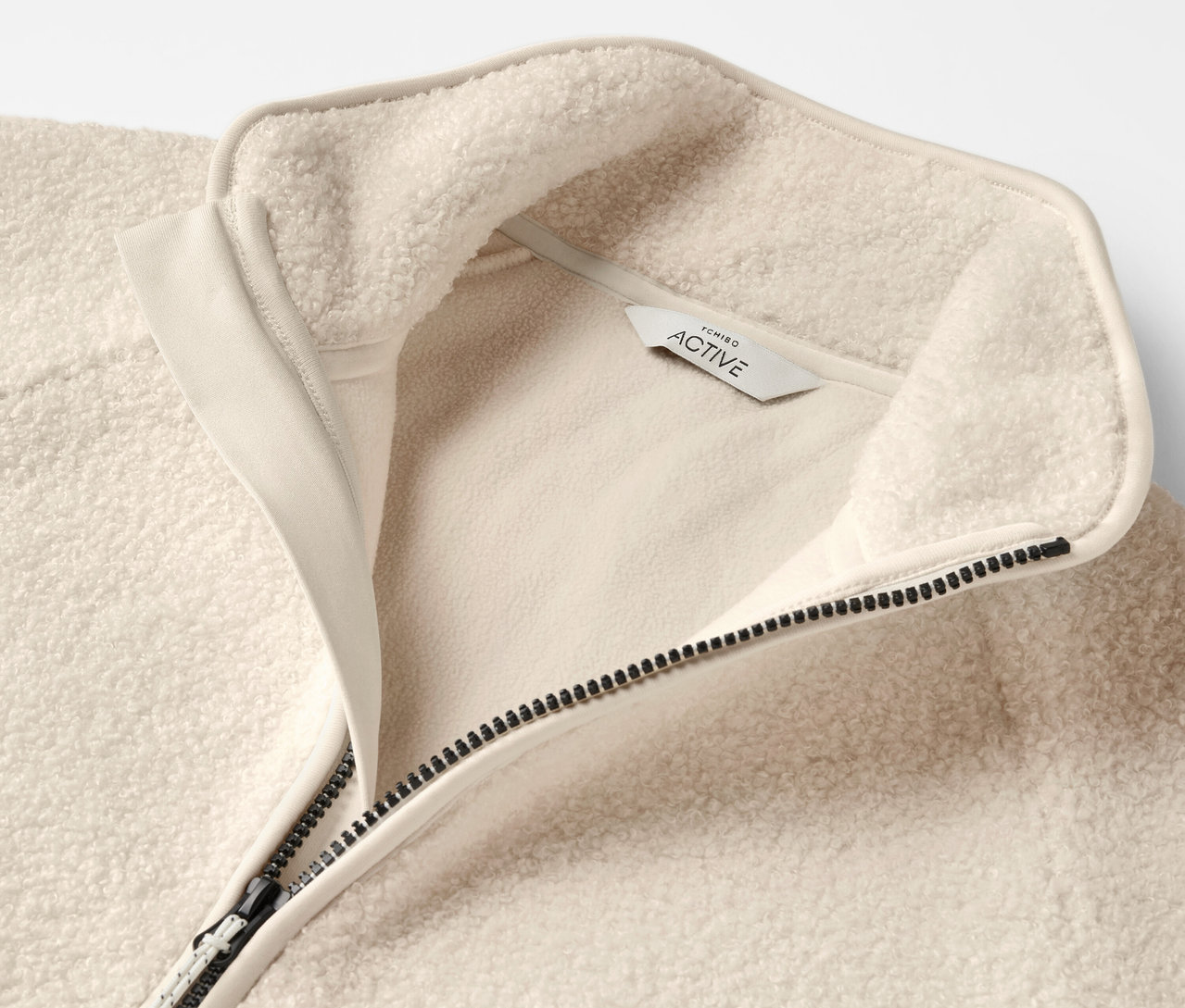 Detailaufnahme einer beigen Fleecejacke mit Reißverschluss und Kragen.