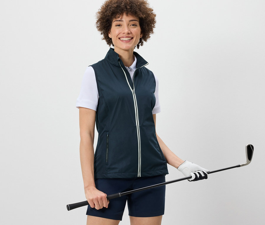 Frau trägt eine Softshellweste und hält einen Golfschläger.