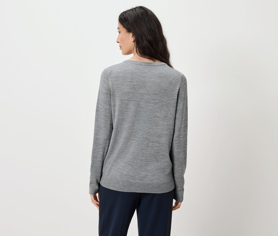 Von hinten ist eine Frau mit langen braunen Haaren zu sehen, die einen grauen Pullover und eine dunkelblaue Hose trägt.