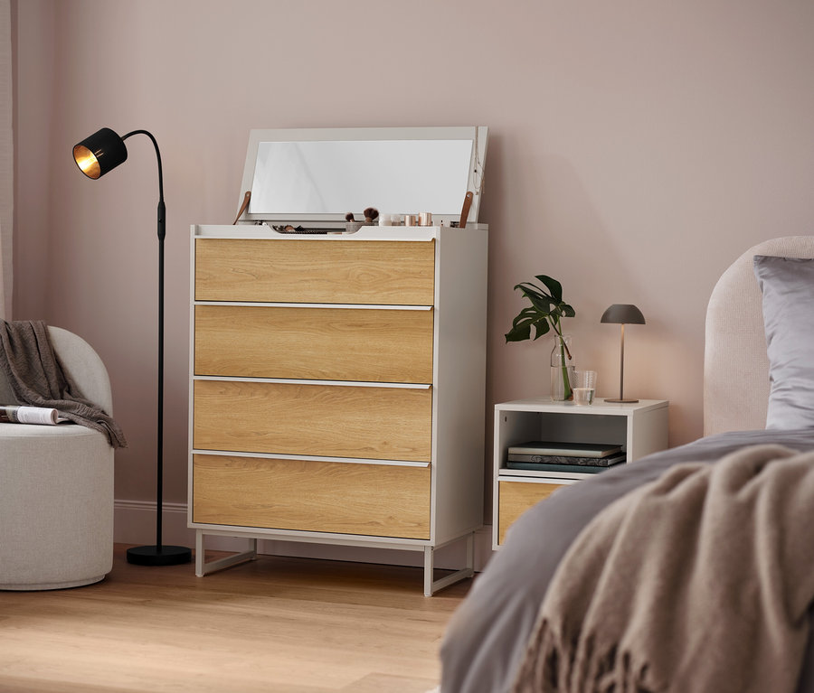 Schlafzimmer mit weißer Kommode mit vier Schubladen, Spiegel und Lampe.