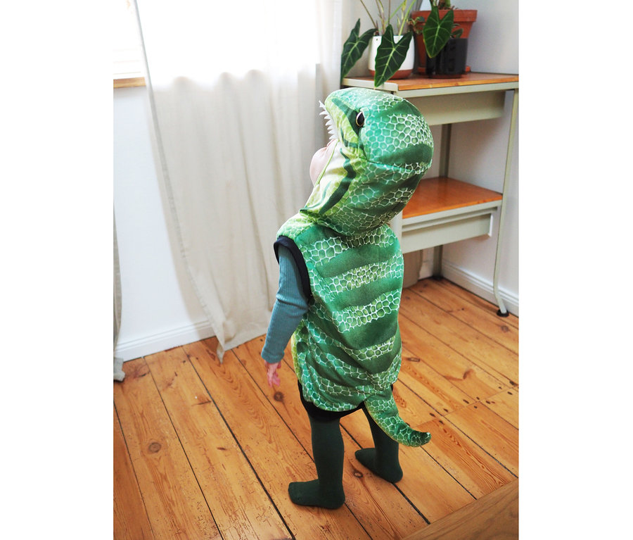 Ein Kind im small foot Kostüm-Weste »Dinosaurier« steht auf einem Holzboden.