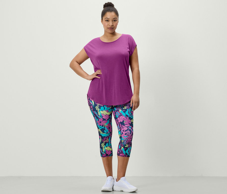 Frau posiert in violettem Sportshirt und 3/4 Sporttight mit Alloverprint.