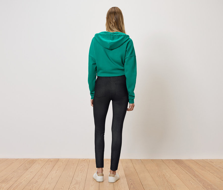 Eine Frau steht mit dem Rücken zur Kamera und trägt einen grünen Hoodie und schwarze Leggings.