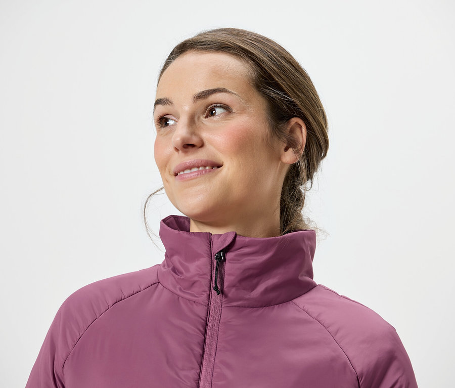 Frau mit braunen Haaren und rosa Jacke blickt nach rechts.