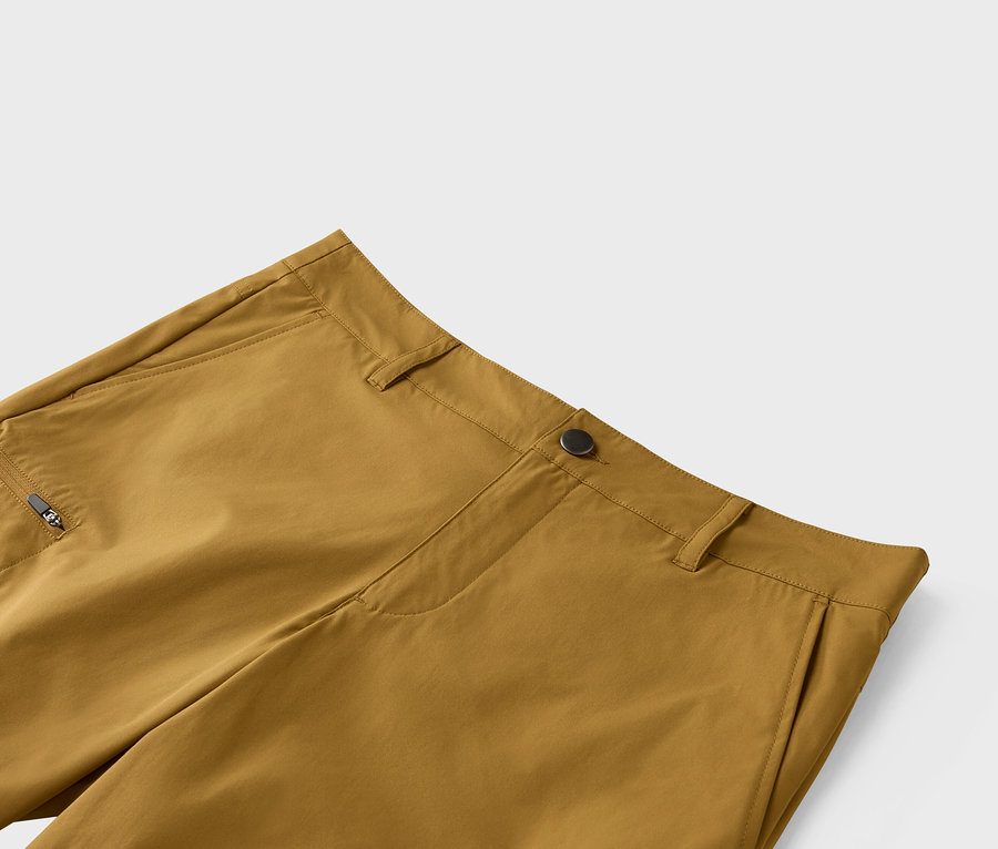 Nahaufnahme einer ockerfarbenen Hose mit Knopfverschluss und Reißverschlusstasche.