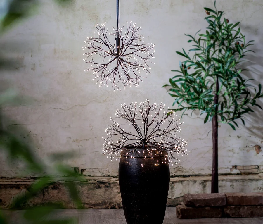 Eine leuchtende Kugeldekoration hängt über einer leuchtenden Dekoration in einer Vase neben einem Baum.