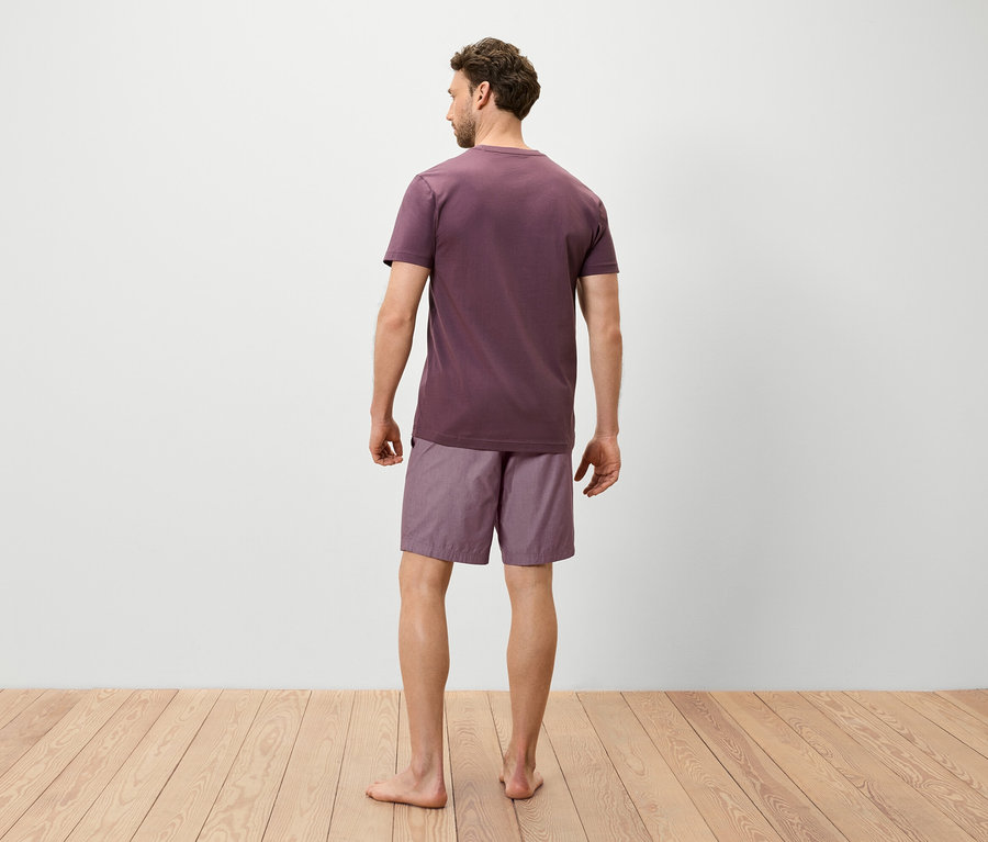 Ein Mann steht mit dem Rücken zur Kamera und trägt ein violettes T-Shirt und Shorts.