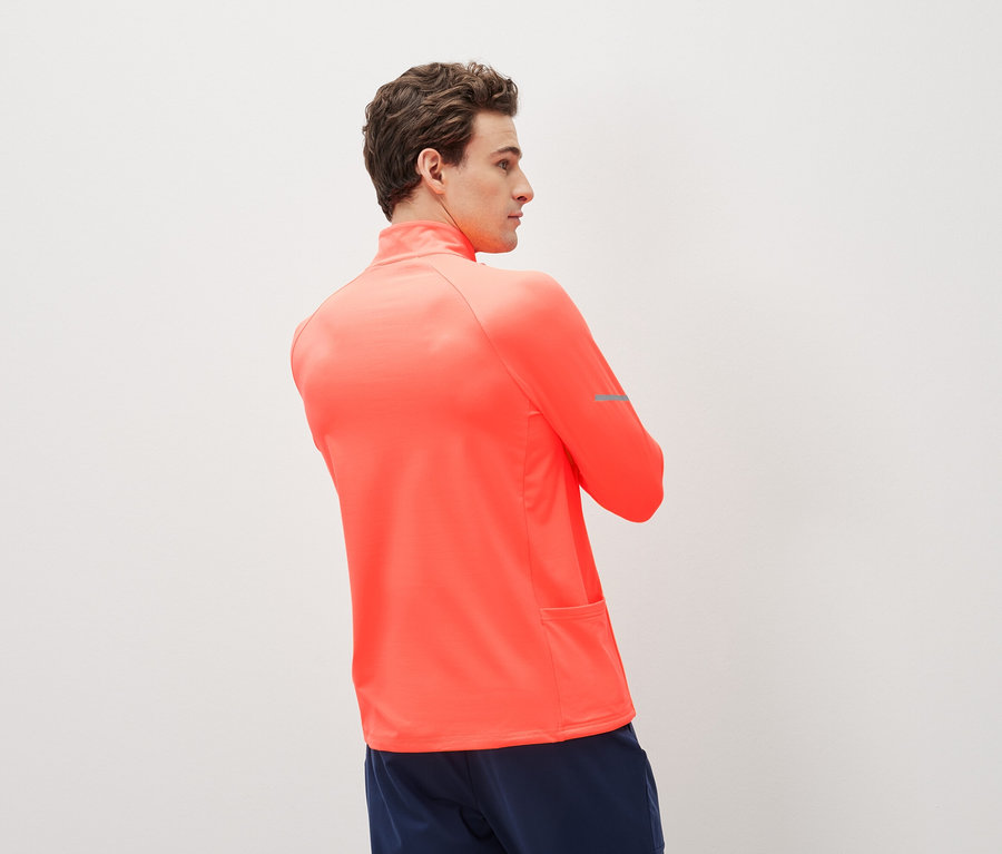 Mann trägt ein korallenrotes Sportoberteil mit langen Ärmeln und dunkelblaue Sportshorts.