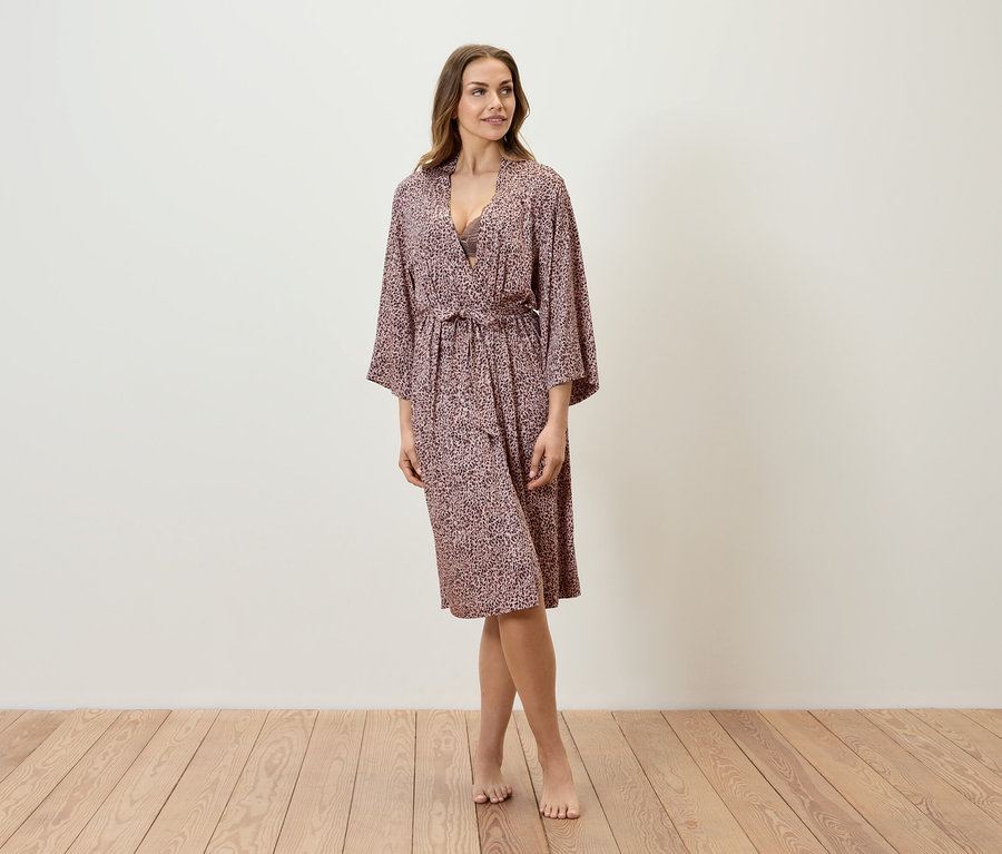 Eine Frau steht auf einem Holzboden und trägt einen gemusterten Bademantel.