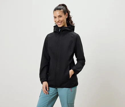 Frau mit Zopf trägt eine schwarze Softshelljacke und blaue Hosen.