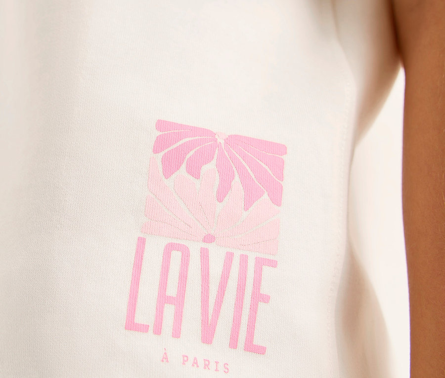 Nahaufnahme eines weißen CECIL Sweatshirts mit einem rosa Grafikdruck, der eine stilisierte Blume über „LAVIE“ und „À PARIS“ zeigt, getragen von einer Person.
