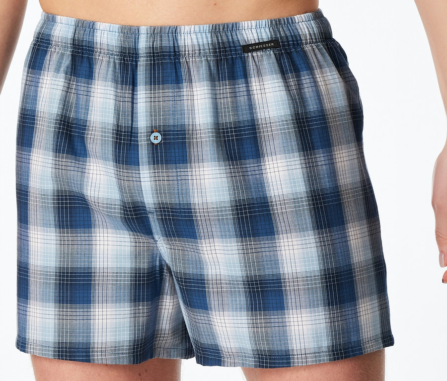 Eine Person trägt blaue und weiße karierte SCHIESSER Web-Boxer mit elastischem Bund und Knopfverschluss.