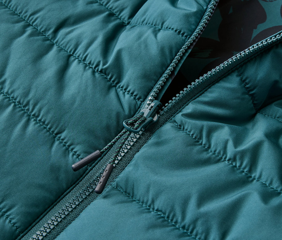 Nahaufnahme einer petrolfarbenen Steppjacke, die teilweise mit einem Reißverschluss geöffnet ist und ein blumiges Innenfutter zeigt.