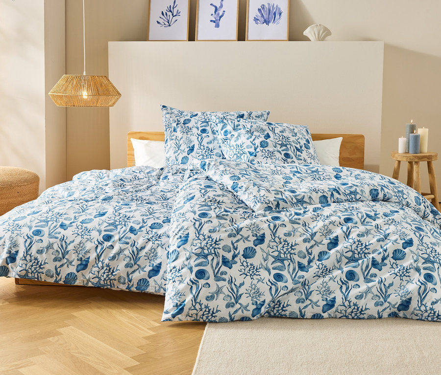 Ein Bett mit blau-weiß gemusterter Bettwäsche steht in einem Schlafzimmer. Über dem Bett hängen drei gerahmte Bilder und eine Lampe.