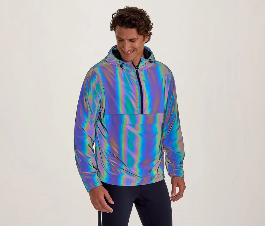Lächelnder Mann in reflektierender, irisierender Kapuzenjacke mit halbem Reißverschluss und Bauchtasche, blickt nach unten.