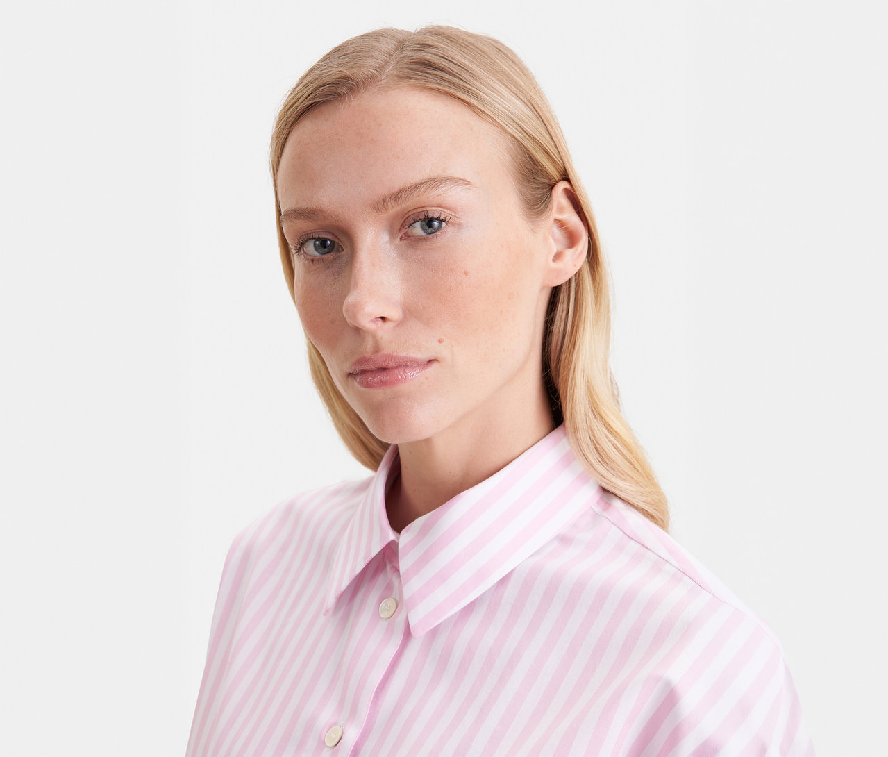 Blonde Frau trägt eine roséfarbene, gestreifte Seidensticker Oversize Hemdbluse und blickt nach vorne.