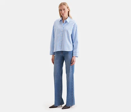 Eine Frau trägt eine blau-weiß gestreifte Seidensticker Oversize Hemdbluse und blaue Jeans.