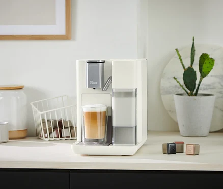Qbo MILK MASTER White Cashmere Kaffeemaschine bereitet Kaffee in einem Glas zu.