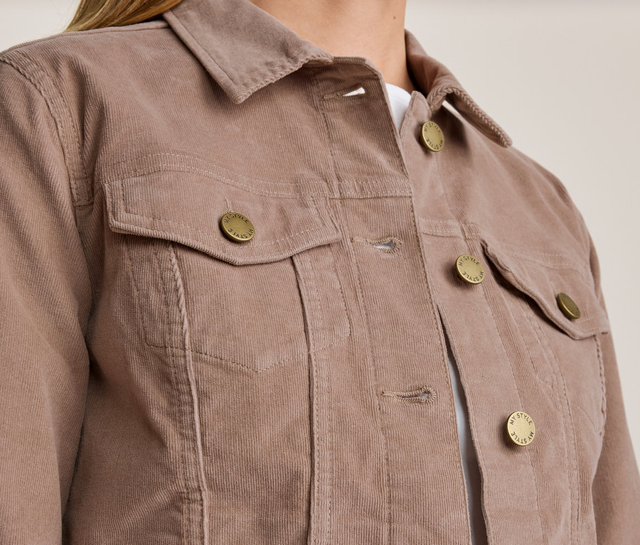 Nahaufnahme einer Person, die eine mauvefarbene Cordjacke trägt. Die Jacke hat einen Kragen, zwei Brusttaschen mit Klappen und goldfarbene Knöpfe mit der Aufschrift 'MY STYLE'.