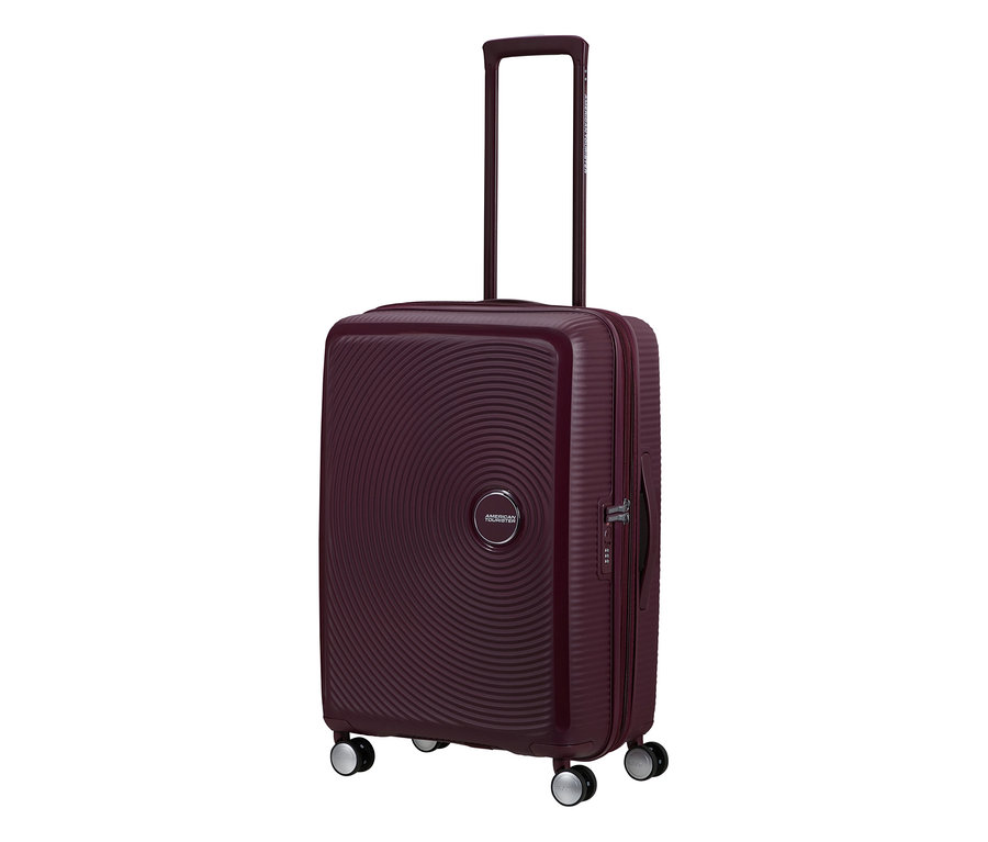 Ein mittelgroßer American Tourister Hartschalen-Koffer »Soundbox« Spinner in Wildkirschrot mit ausgefahrenem Teleskopgriff und vier Rollen.