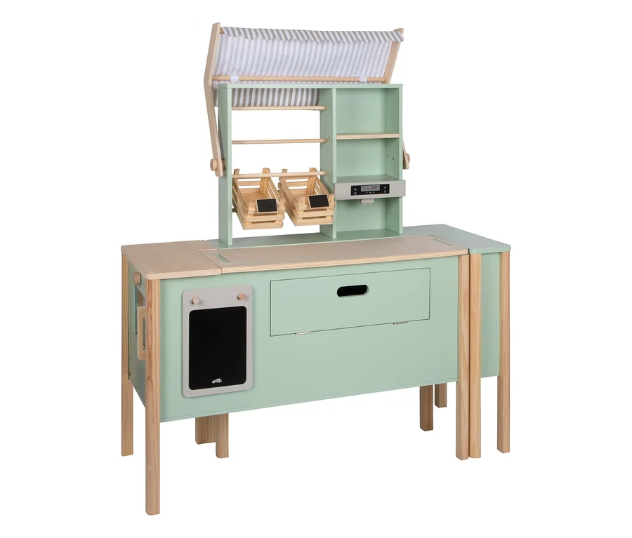 Ein hellgrüner und naturfarbener small foot „fresh“ Kaufladen und Kinderküche, mit gestreiftem Vordach, Regalen, zwei hängenden Körben, einer Spielzeugkasse, einer Schublade und einer Tafel.