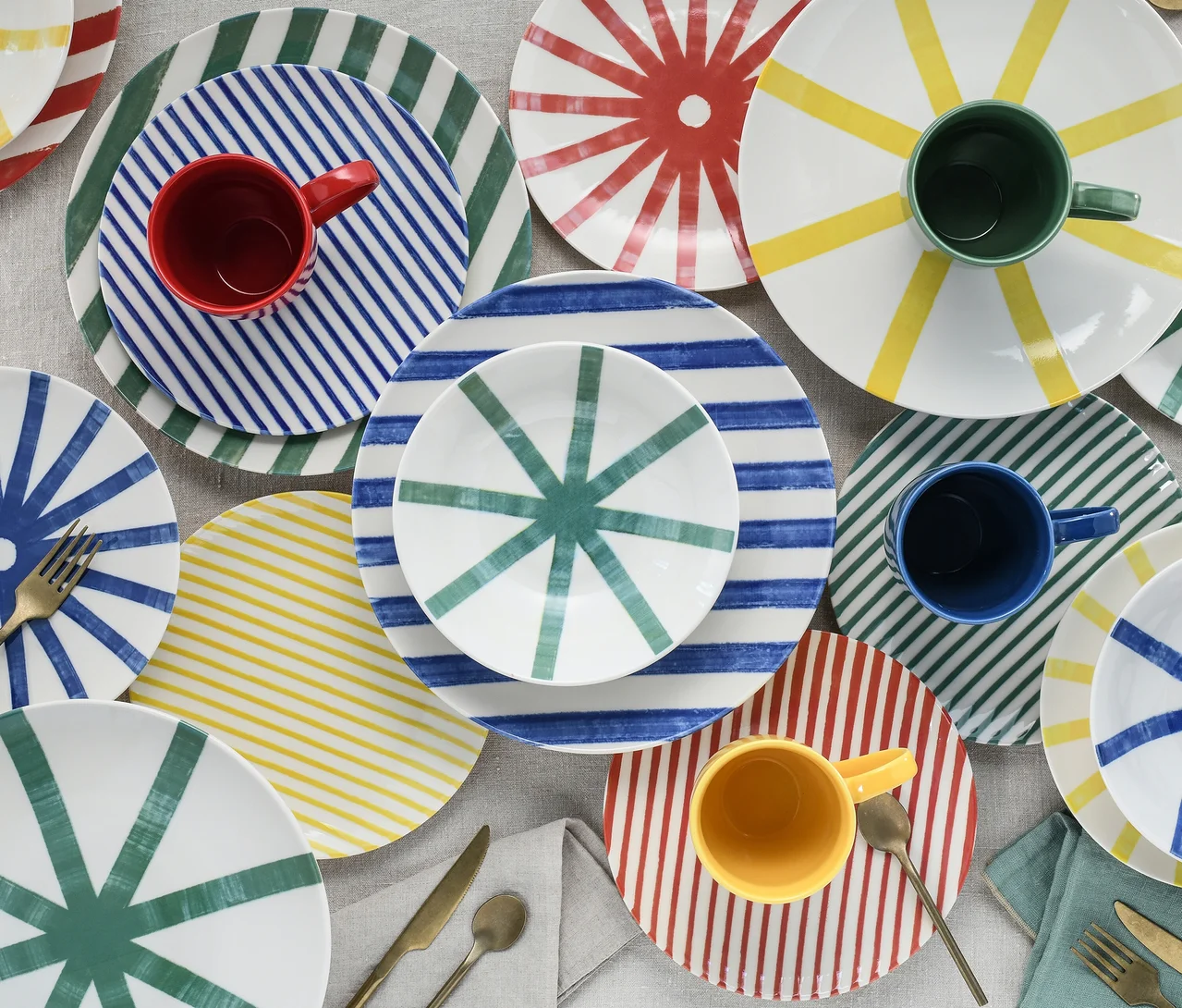 Buntes creaTable Teller-Setet, 16-teilig, mit Tellern, Schalen und Tassen in Rot, Blau, Grün und Gelb mit Streifen- und Sternmustern, auf einem Tisch mit Besteck und Servietten.