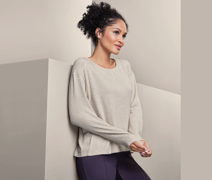 Frau lehnt an Wand und trägt einen Sweat-Pullover und Leggings.