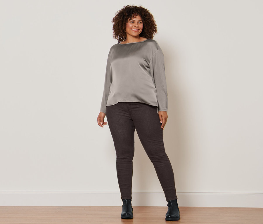 Frau posiert in Blusenshirt im Materialmix, dunkelbraunen Treggings und Lederboots.