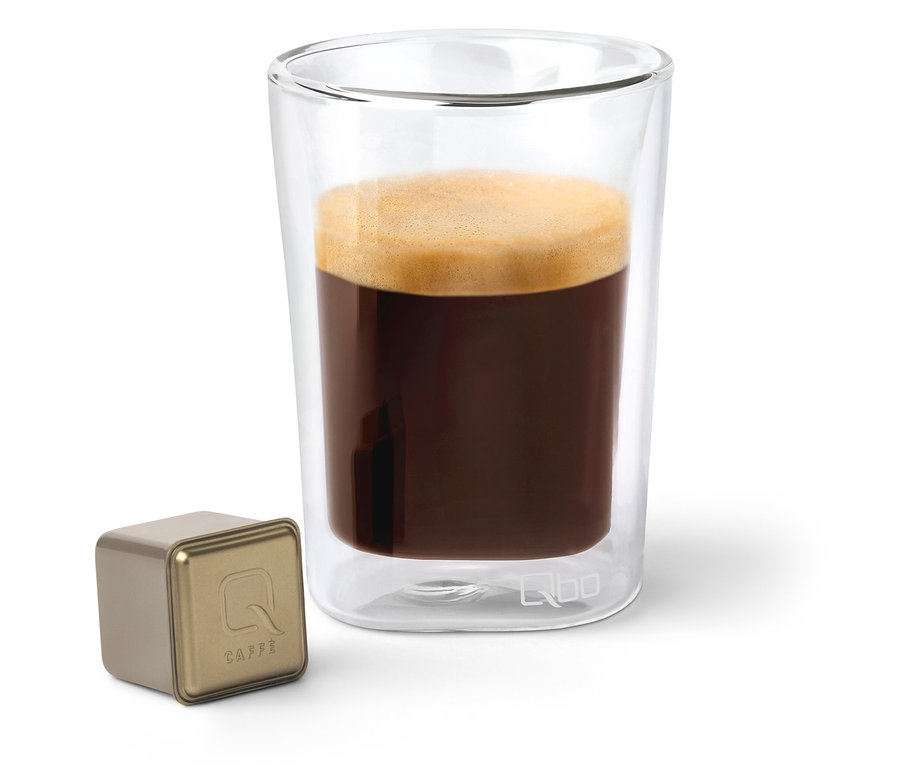 Eine Qbo Caffè JABANA YIRGA Kapsel neben einem Glas Kaffee.