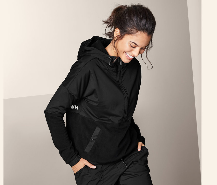 Frau trägt einen schwarzen Hybrid-Fleecesweater und eine schwarze Hose.