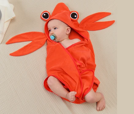 Baby liegt in Krabbenform Kapuzenhandtuch gewickelt auf Decke.