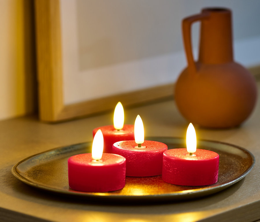 Vier rote LED-Echtwachs-Teelichter auf einem goldenen Tablett auf einem Schrank.