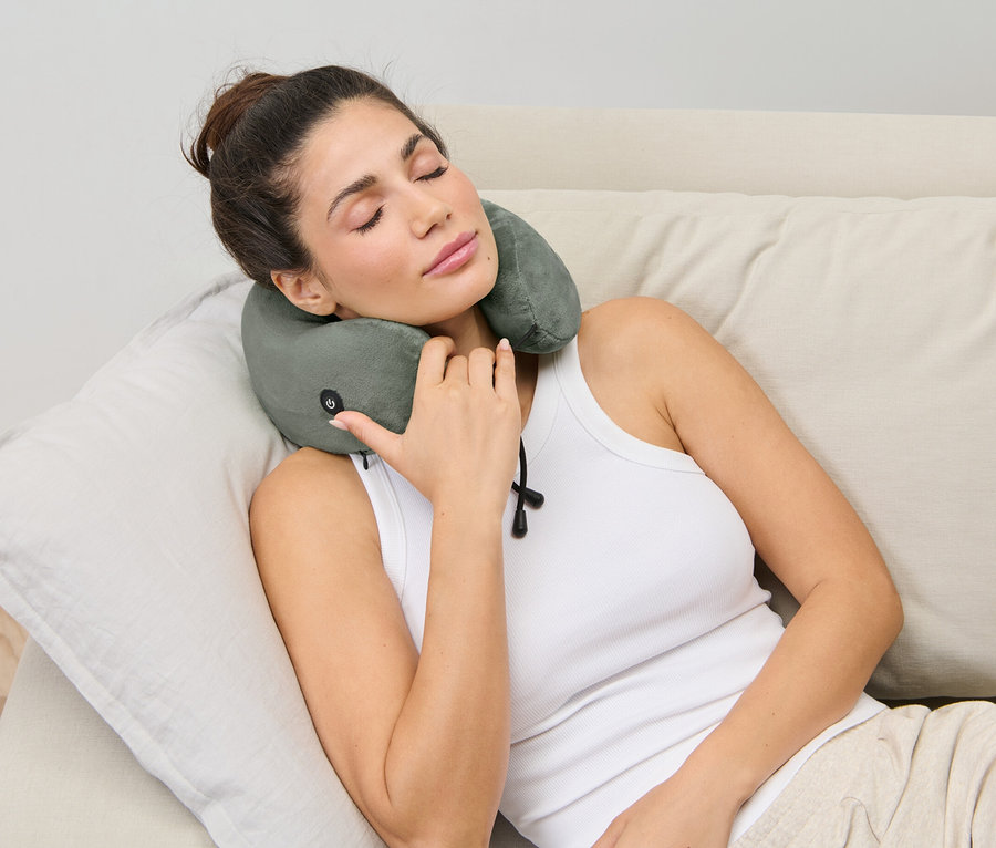Frau liegt mit Nackenkissen mit Vibrationsmassage auf der Couch.