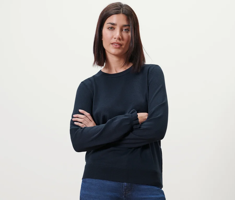 Frau posiert mit verschränkten Armen in Feinstrickpullover mit Rüschendetail, dunkelblau.