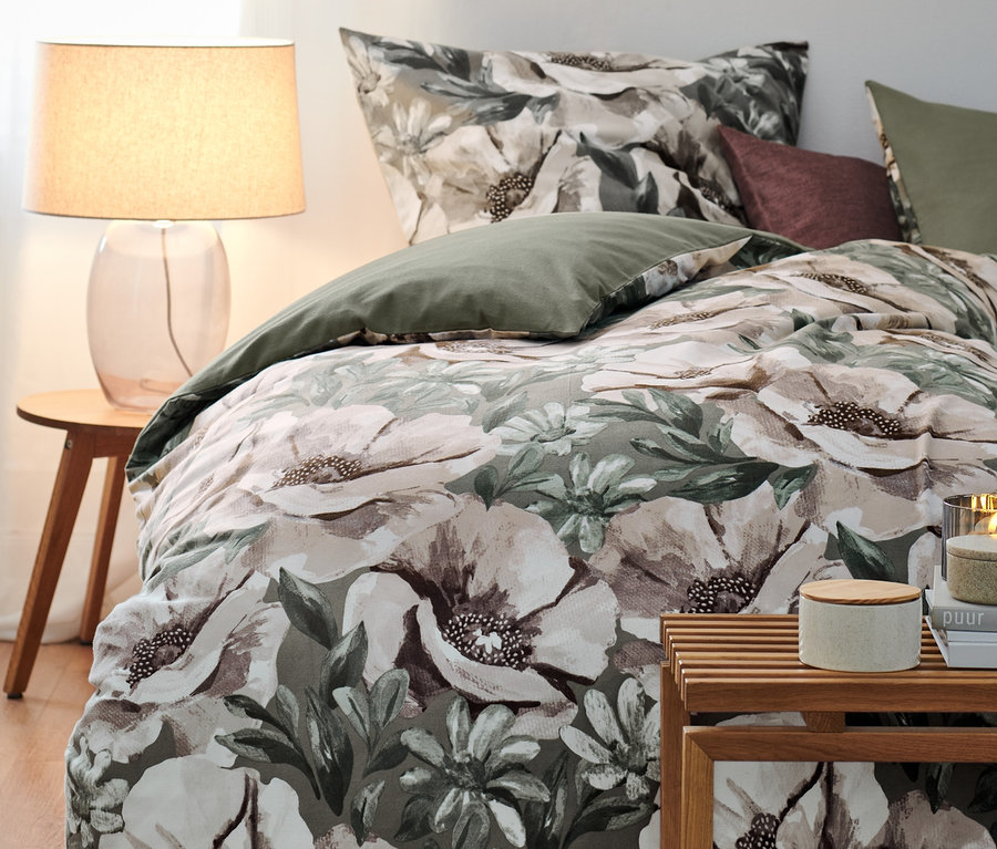 Biber-Bettwäsche mit Blumenmuster liegt auf einem Bett neben einer Lampe und einem Tisch.