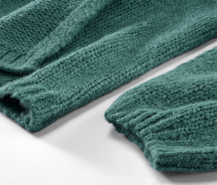 Detailansicht eines offenen, grob gestrickten, grünen Cardigans.