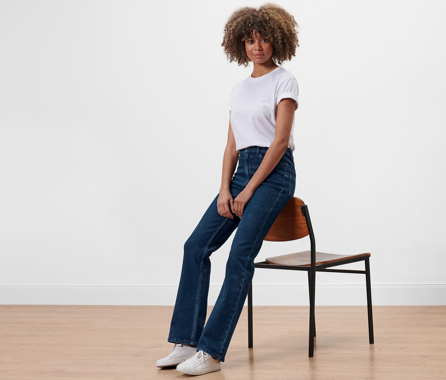 Frau sitzt auf einem Stuhl und trägt eine Bootcut-Denim »Fit Lou«.