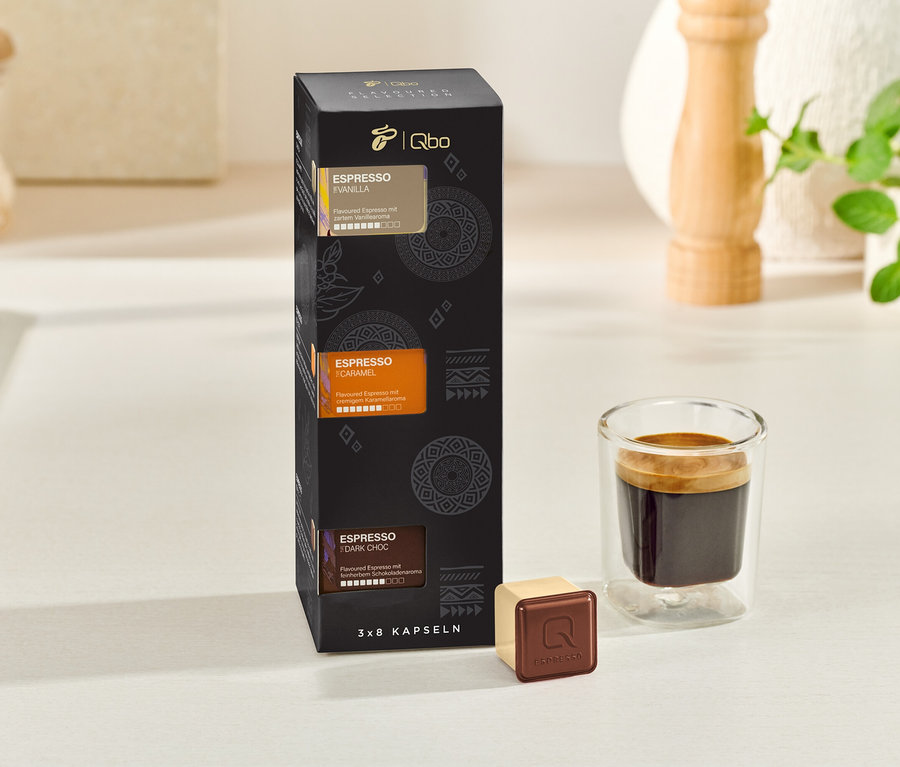 Eine schwarze Schachtel Qbo Espresso Kapseln neben einer Tasse Espresso.