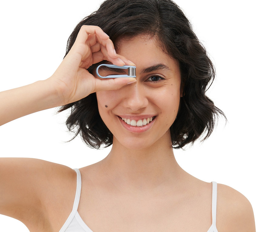 Frau lächelt und hält einen manuellen Mini-Gesichtshaarentferner vor ihr Auge.