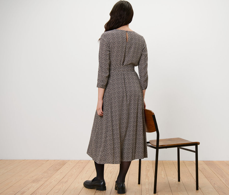 Frau steht mit dem Rücken zur Kamera und trägt ein bedrucktes Webkleid.