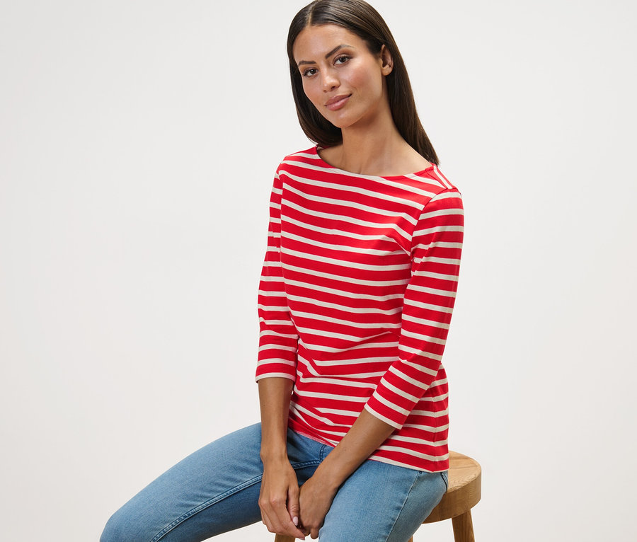 Frau sitzt auf einem Hocker und trägt ein gestreiftes Shirt mit 3/4-Arm, rot getreift.