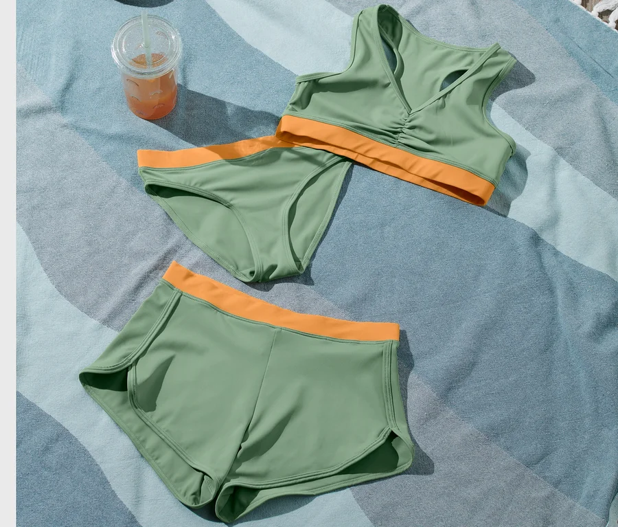 Ein Kinder-Bikini-Set, 3-teilig, ein Getränk und eine Strandtasche liegen auf einem Strandtuch.