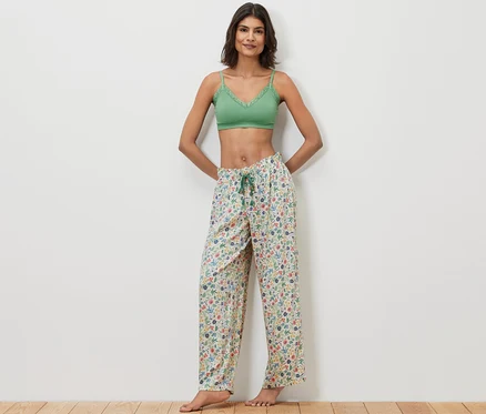 Frau posiert in grünem Spitzen-Bralette und Relaxhose mit Blumenmuster.