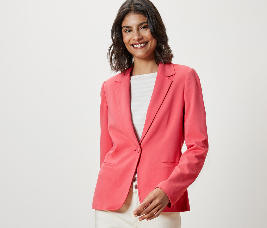 Lächelnde Frau trägt einen korallenroten Jerseyblazer.