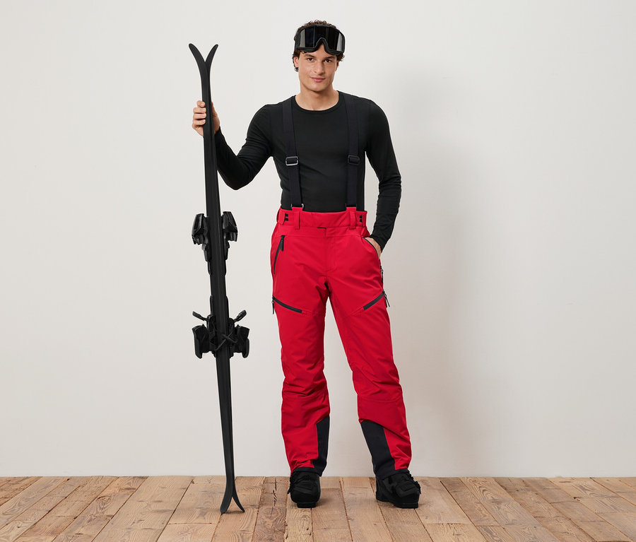 Mann in schwarzem Hemd und roter Skihose, der schwarze Skier hält.