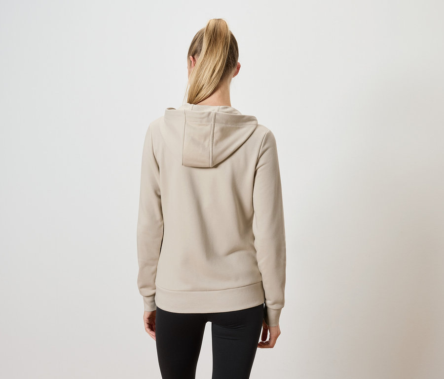 Rückansicht einer Frau mit blonden, zu einem Pferdeschwanz gebundenen Haaren, die einen beigen Kapuzenpullover und eine schwarze Hose trägt.