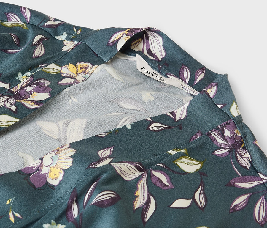 Detailaufnahme eines grünen Bademantels mit Blumenmuster und weißem Saum.