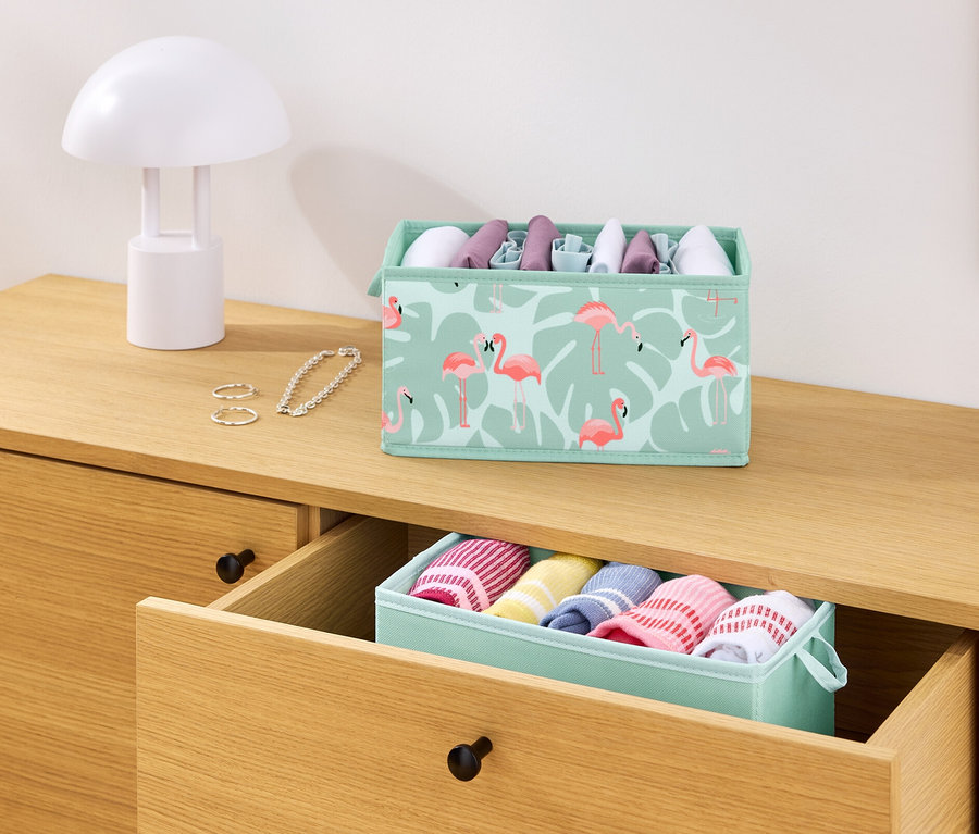Auf einer Kommode stehen 2 Schubladen-Ordnungsboxen, eine mit Flamingos und eine mit Kleidung.