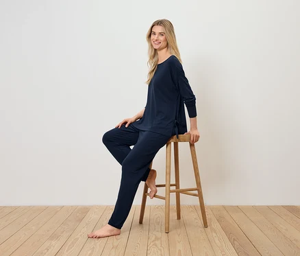 Blonde Frau sitzt auf einem Holzhocker und trägt einen dunkelblauen Pyjama.