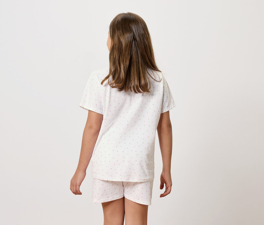 Mädchen im kurzärmeligen Pyjama mit Shorts steht mit dem Rücken.